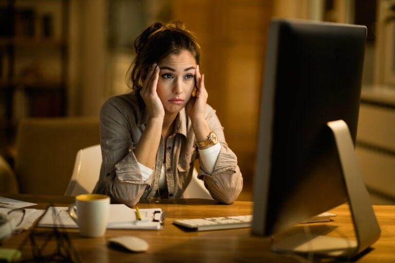 Young woman sits confused in front of a laptop.