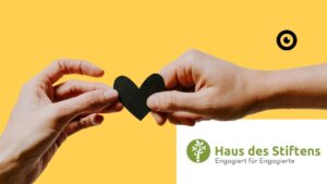 Dos manos sostienen juntas un corazón negro. Debajo aparece la firma: Haus des Stiftens - Engagiert für Engagierte